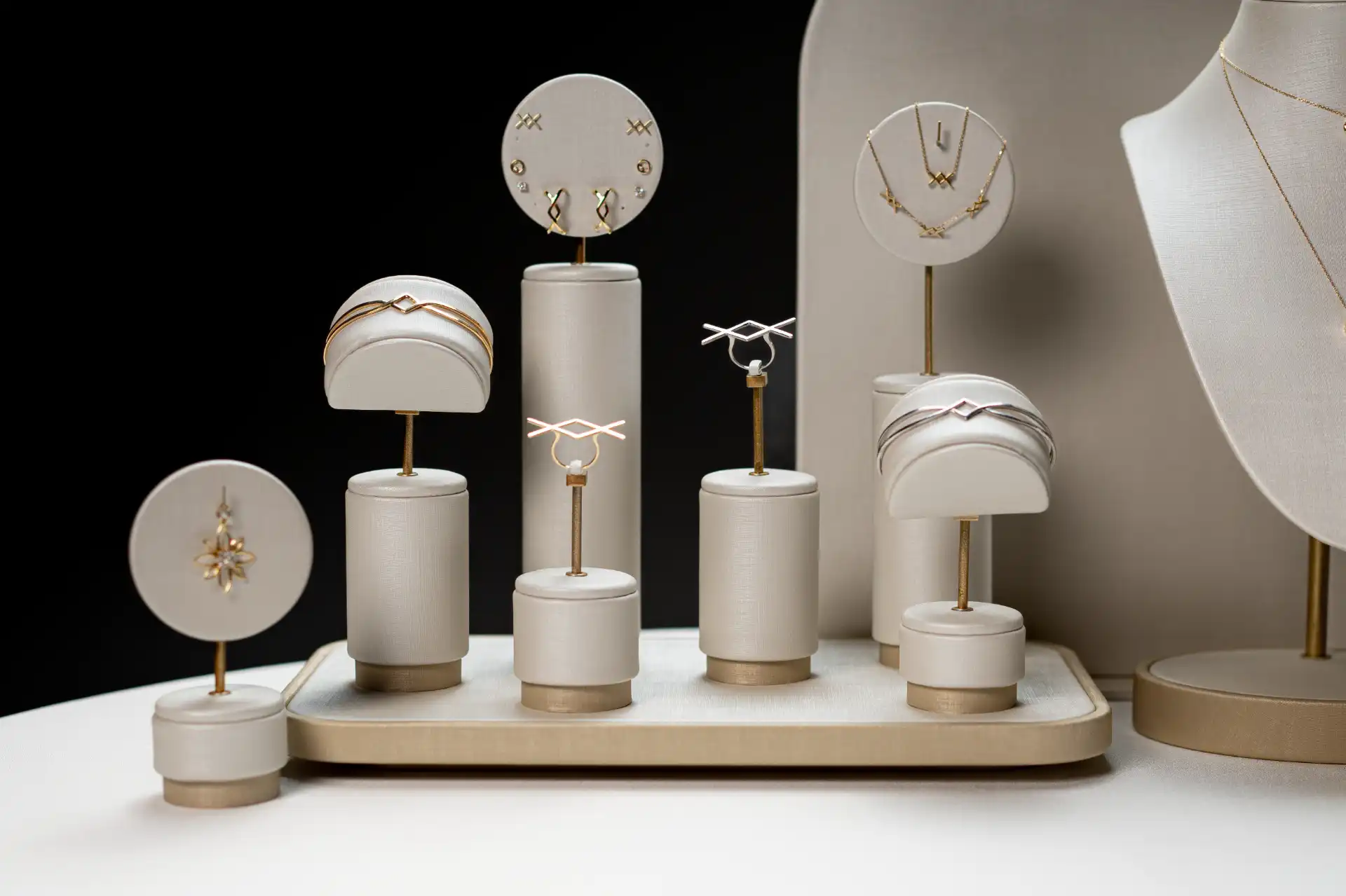 Exposição de joias minimalistas em uma vitrine com fundo preto, incluindo brincos, colares e anéis com design elegante e sofisticado.